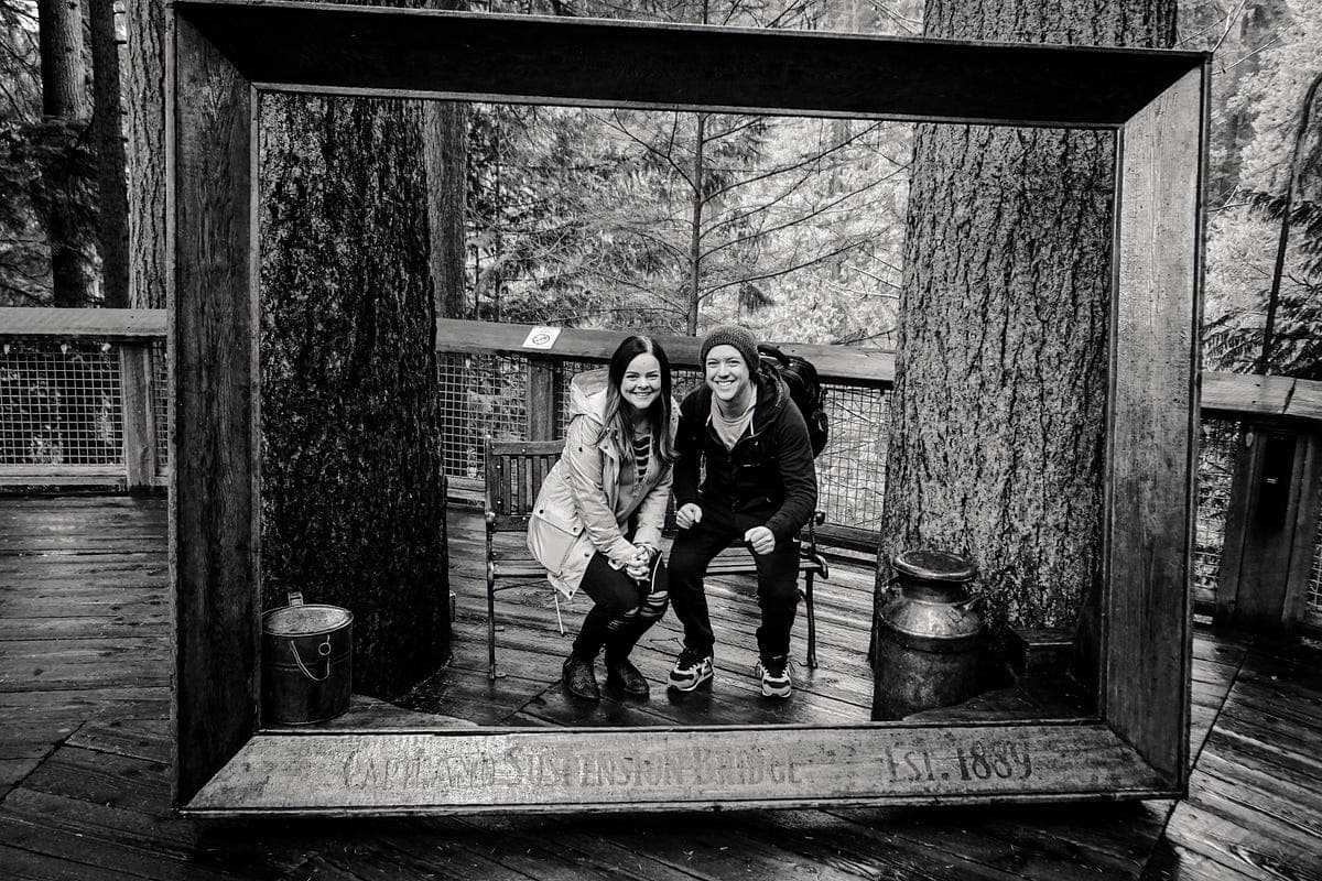 A couple posing in a wooden frame on a forest suspension bridge