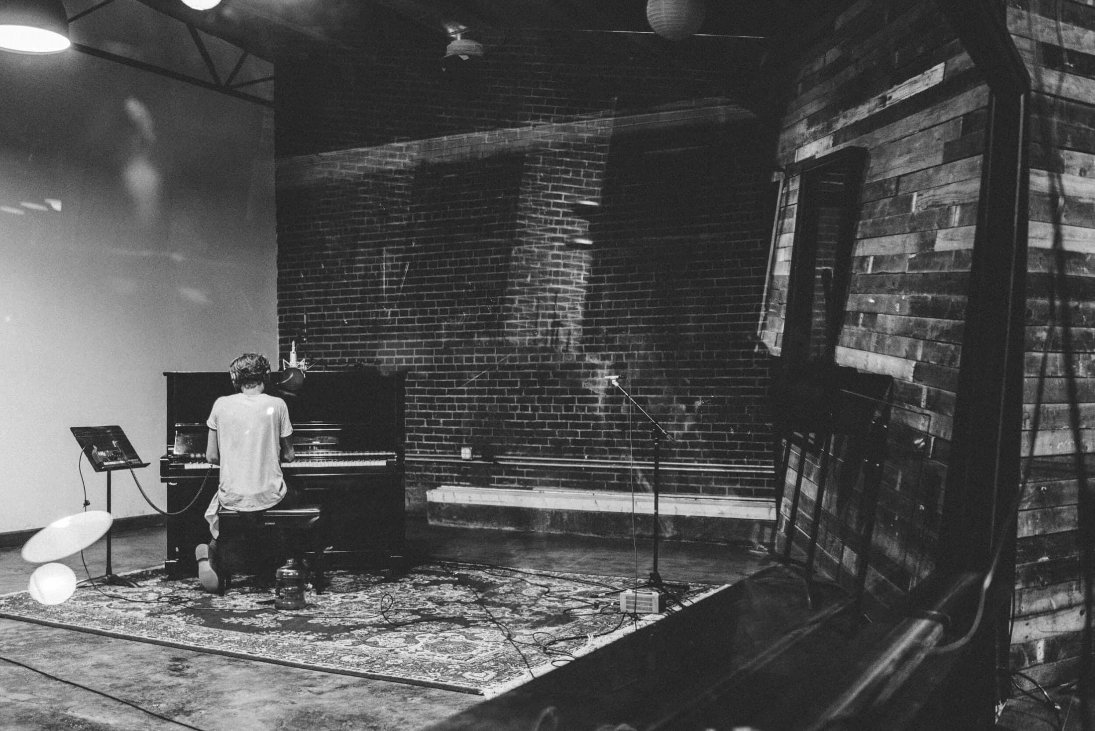 Black-and-white photograph of a musician recording at an upright piano in Studio A