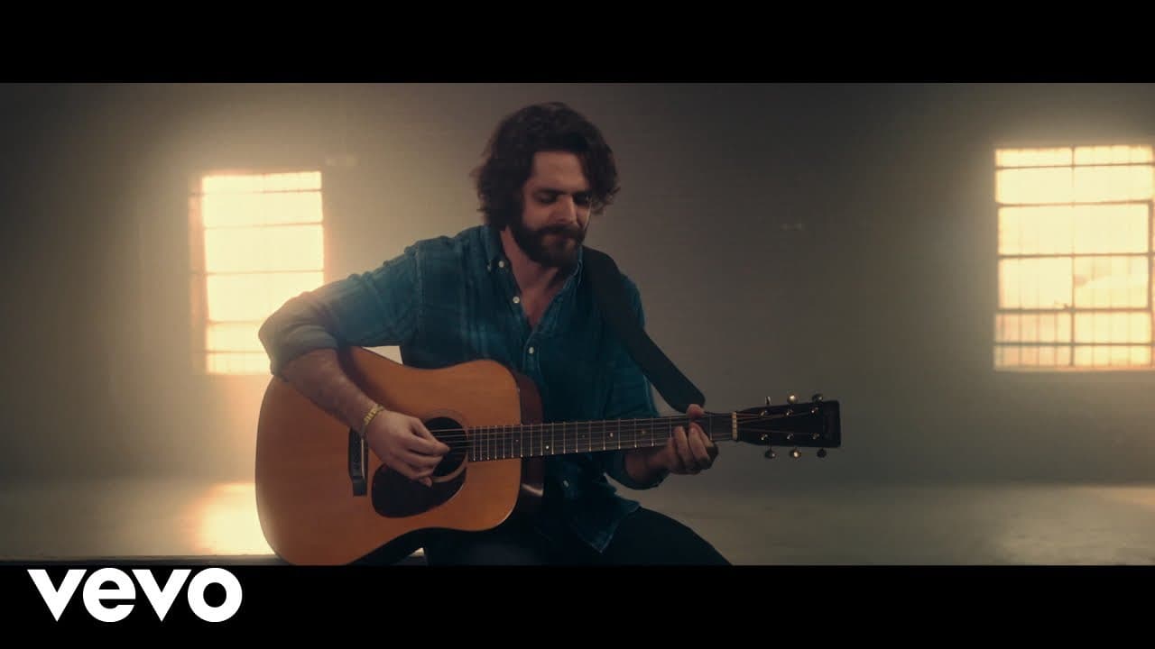 Thomas Rhett playing acoustic guitar in warm light from two high Warehouse windows.