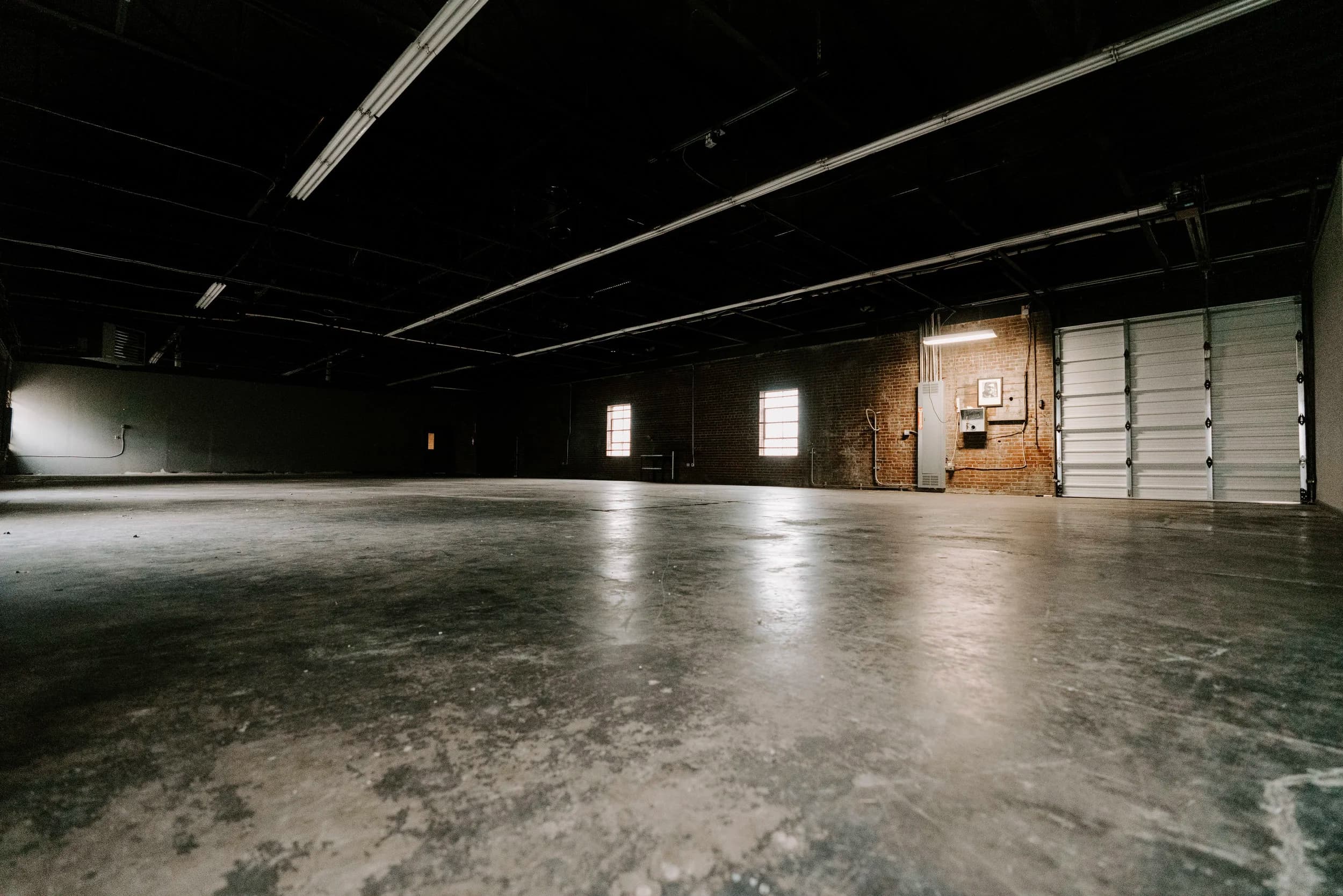 The open Warehouse at South x Sea, with concrete floors, exposed brick, high windows, and a roll-up door.