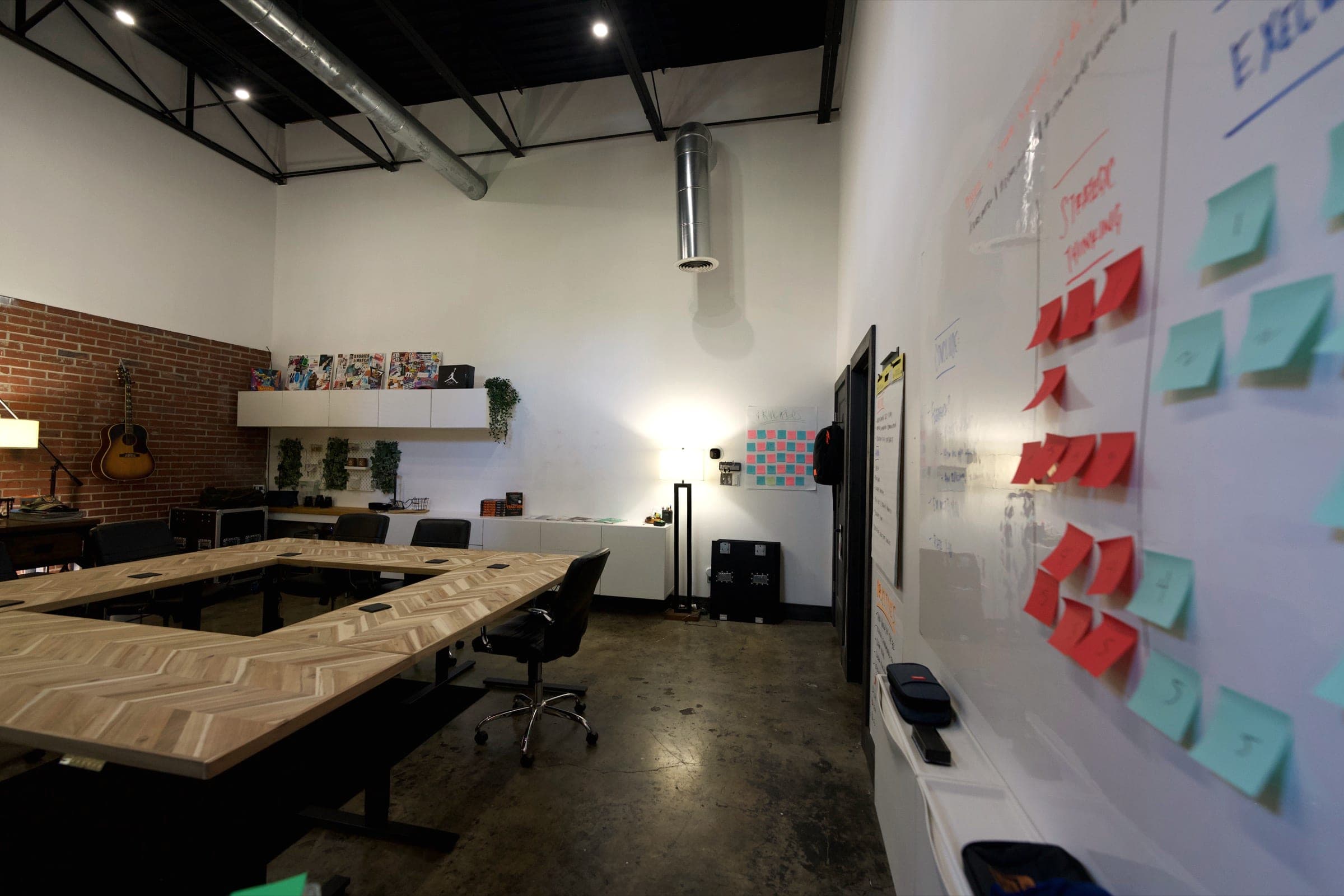 Herringbone tables fill an exposed-brick session room with a wall of sticky notes at right.