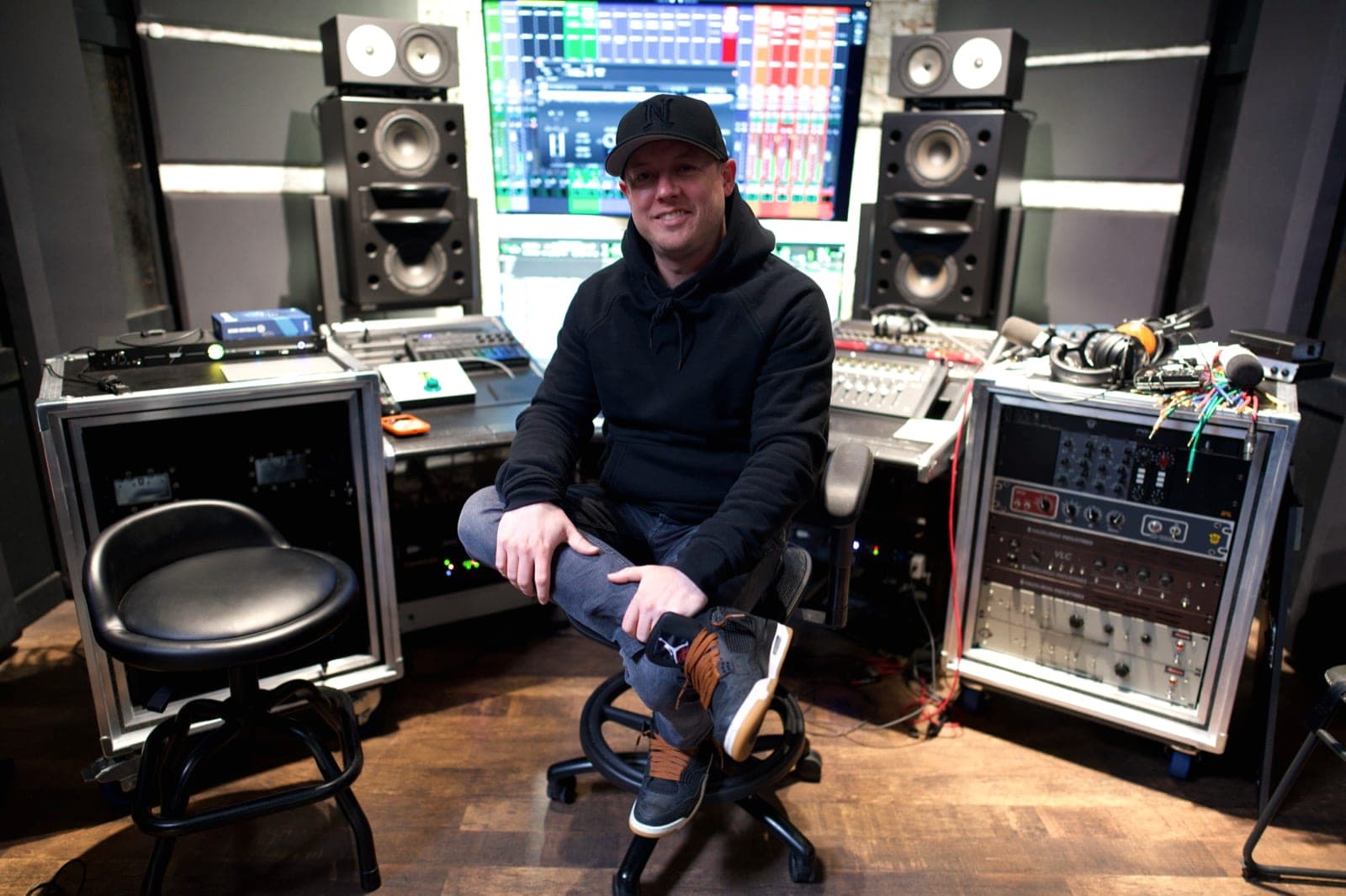 Brandon Metcalf sits between two equipment racks with the control-room monitors lit behind him.