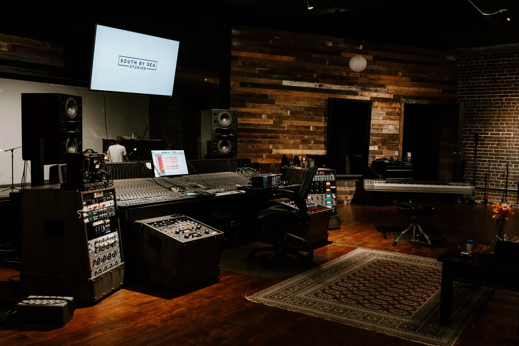 Studio A at South x Sea, with the recording console, wood-paneled walls, exposed brick, and a view into the live room.